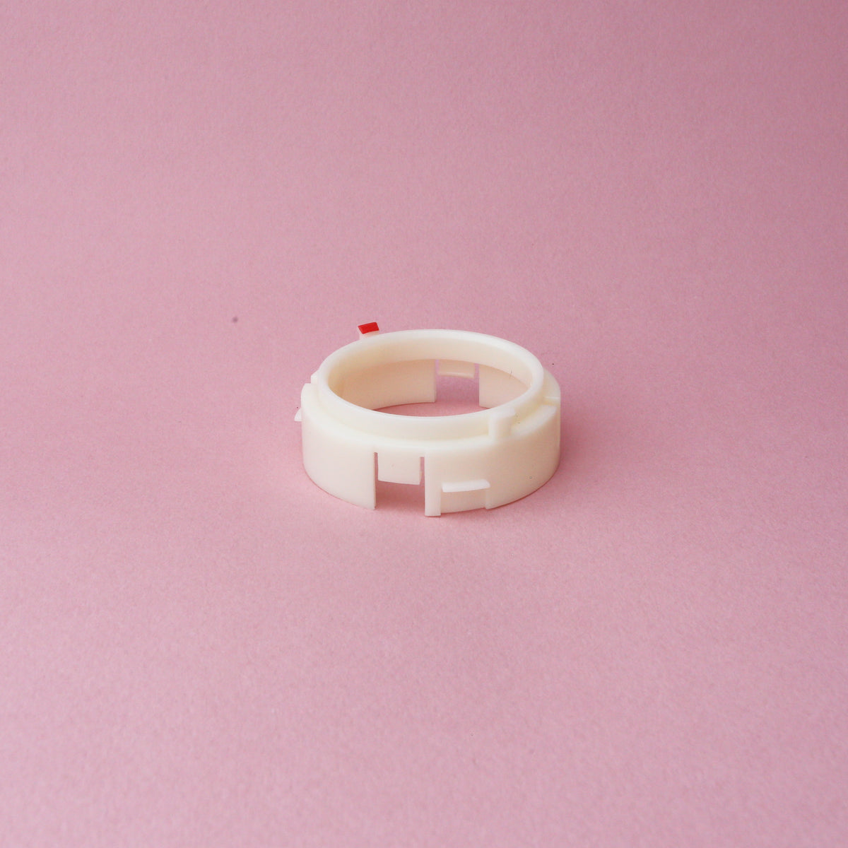 A white plastic Tandem Coffee Roasters Baratza Ring Burr Holder with small notches sits on a pink background.