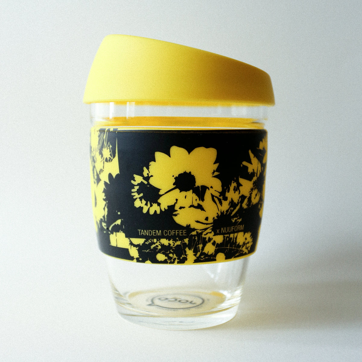 The Tandem x NUUFORM Joco Cup by Tandem Coffee Roasters is a plastic-free, reusable borosilicate glass cup with a yellow lid and black sleeve featuring bright yellow floral art from an artist collab, and "Tandem Coffee x MiiR" printed on the sleeve.