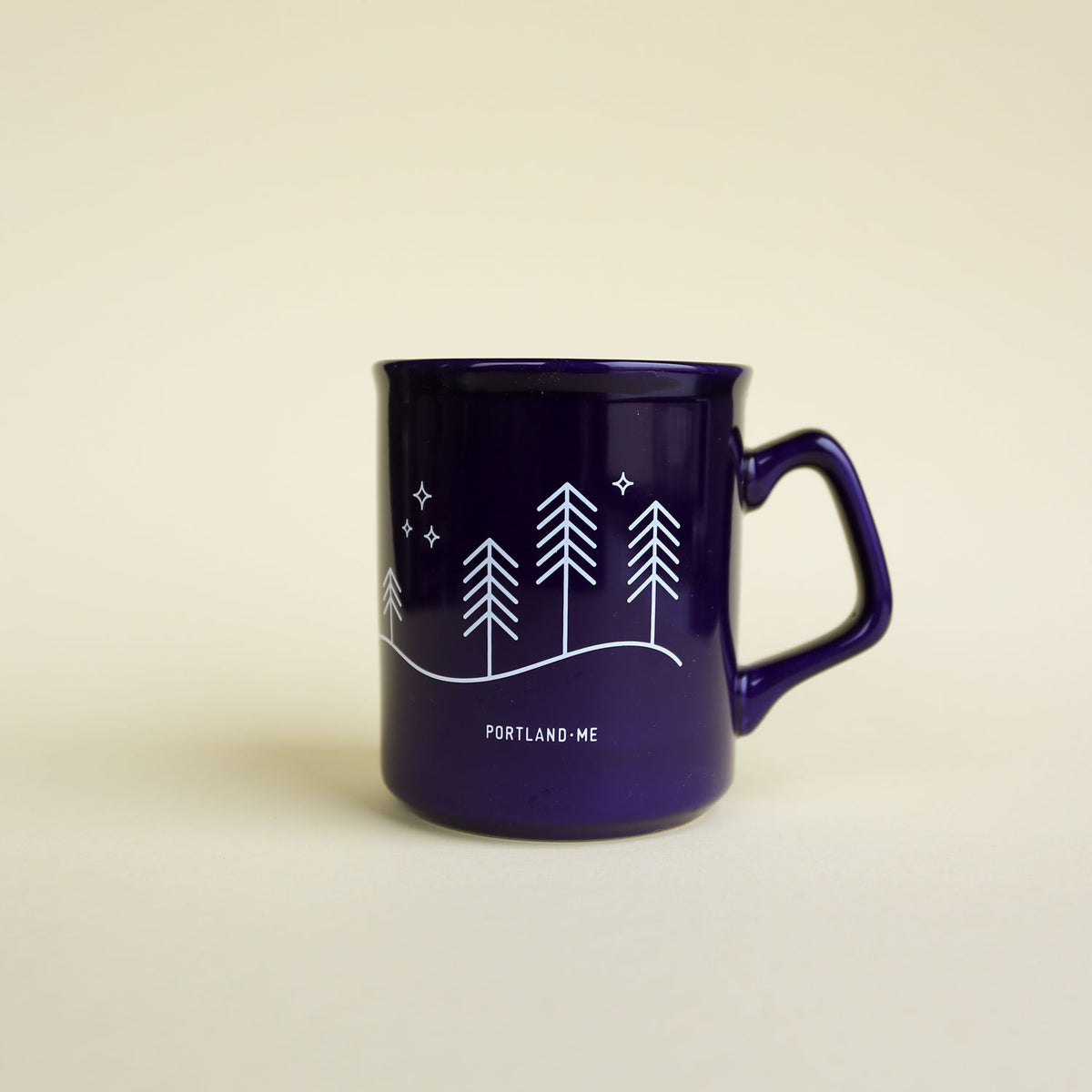 The Moon & Stars Mug by Tandem Coffee Roasters features dark purple with white line art of pine trees, hills, stars, and PORTLAND · ME beneath the design, displayed on a light beige background.