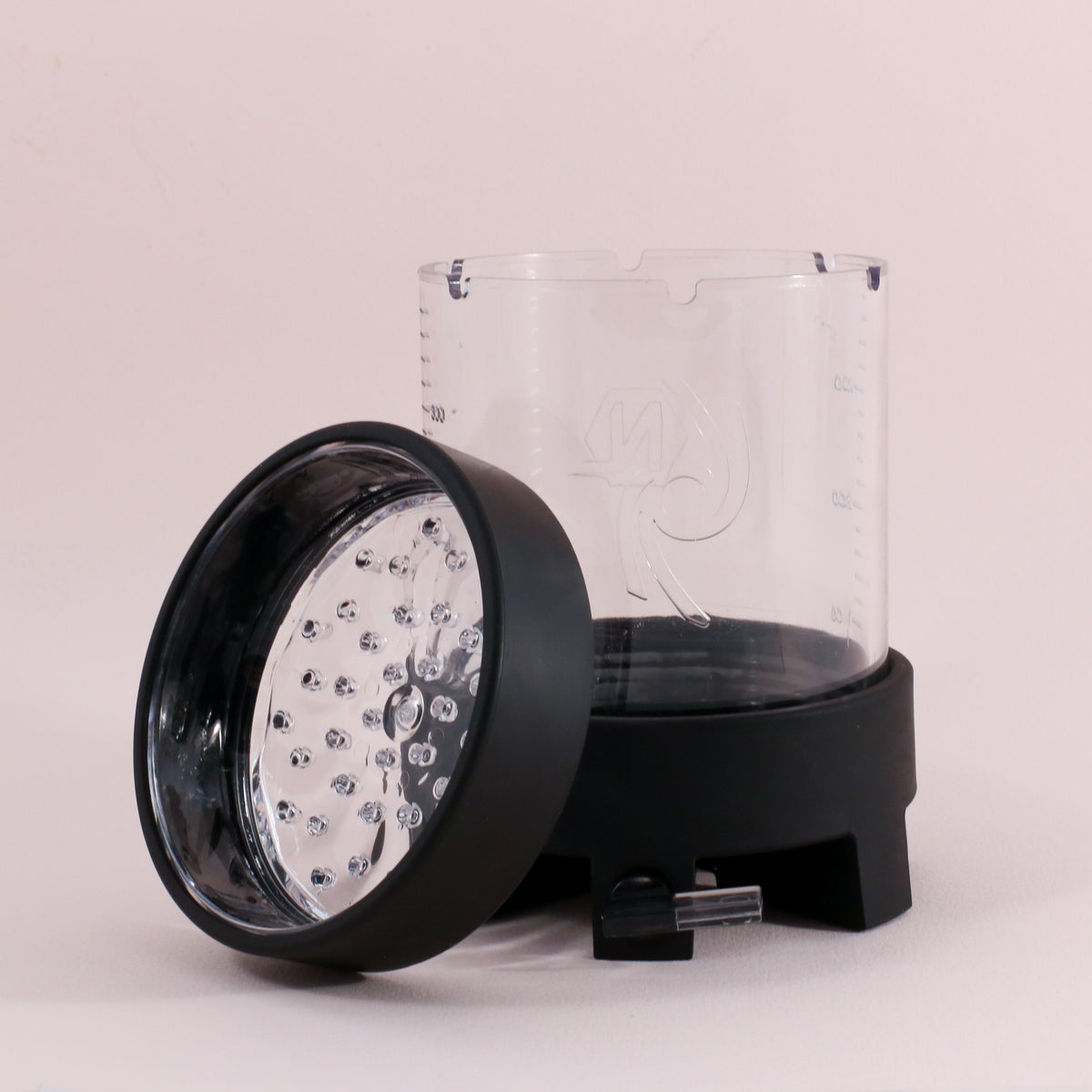 The Tandem Coffee Roasters NextLevel Pulsar Brewer’s transparent pitcher with measurement markings stands upright, while its black and silver blade assembly lid with an adjustable flow valve rests tilted against it on a plain background.